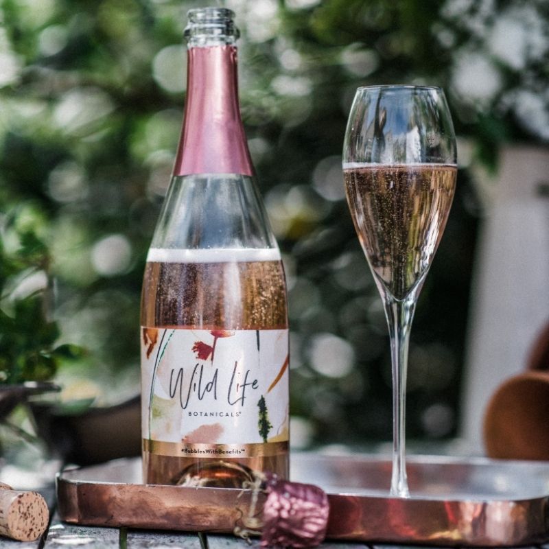 Wild Life Botanicals Blush 75 open bottle on table with full glass of fizz. Ultra-low alcohol, low calorie and low carb sparkling wine. Healthy wine alternative. 