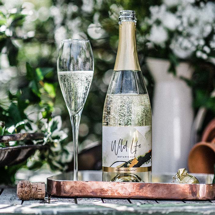 Wild Life Botanicals Nude open bottle on table with full glass of fizz. Ultra-low alcohol, low calorie and low carb sparkling wine. Healthy wine alternative. 