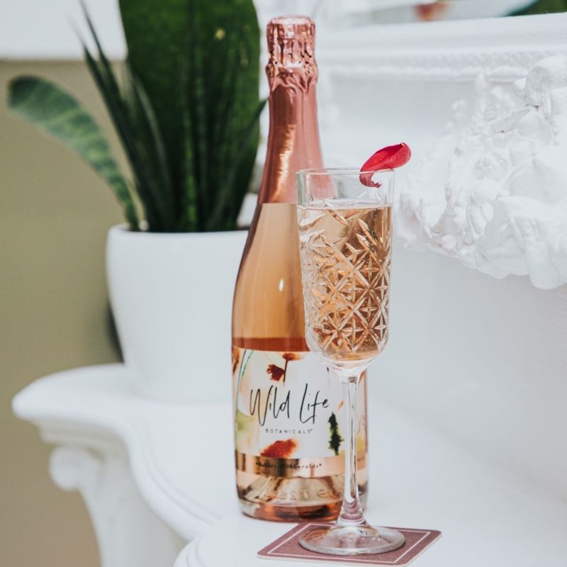 Wild Life Botanicals Blush 75 open bottle on table with full glass of fizz. Ultra-low alcohol, low calorie and low carb sparkling wine. Healthy wine alternative. 